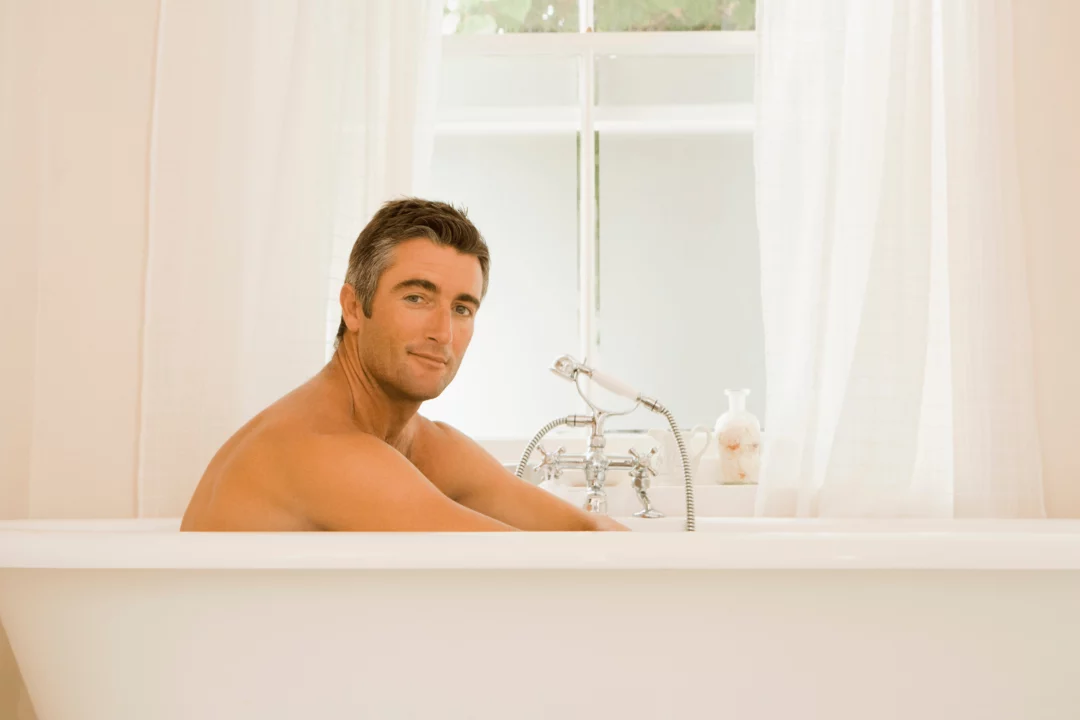 muz relaxuje ve vane v koupelne s bilymi zavesy klidna atmosfera domaciho wellness