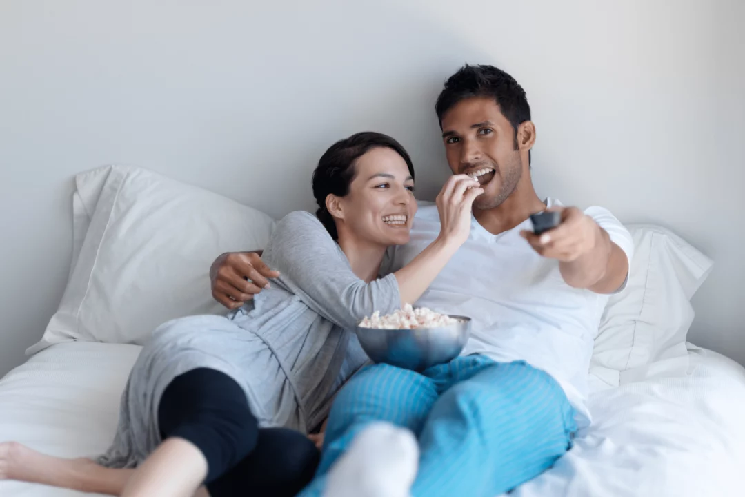 par sleduje televizi v posteli ji popcorn a drzi dalkovy ovladac pohodlne domaci relaxovani a zabava