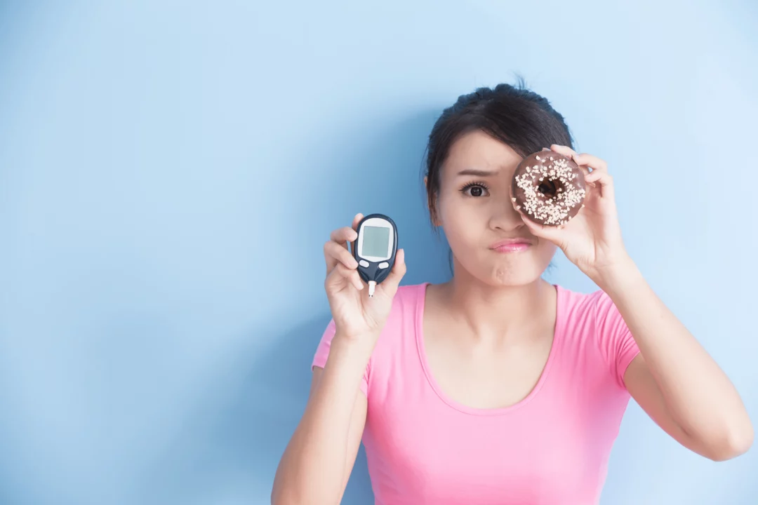 zena s donutem a glukometrem na modrem pozadi vyjadrujici dilema mezi sladkostmi a kontrolou cukru