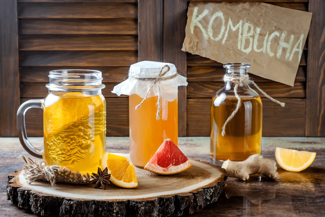 domaci kombucha v sklenicich s citrusy a zazvorem na drevenem podnosu rucne psany napis kombucha v pozadi